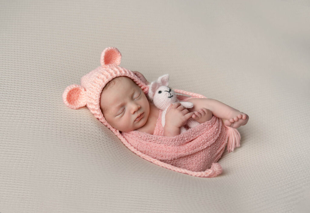 Vale of Glamorgan newborn photographer image of baby in pink knitted wrap and bear hat holding toy – Shutter Hire photography studio in the Vale of Glamorgan.